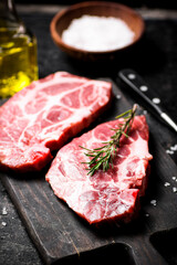 Raw pork steak on a cutting board with rosemary. 