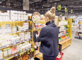 Woman buying make up at cosmetics section in store. choosing cosmetics, perfumes, creams and shampoos, Using tester.