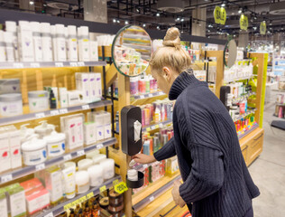 Woman buying make up at cosmetics section in store. choosing cosmetics, perfumes, creams and shampoos, Using tester.