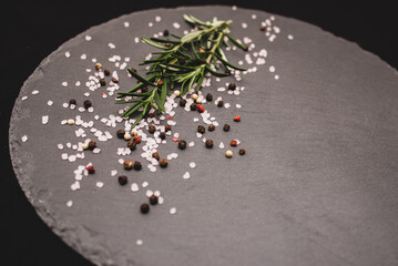 Rosemary herb with pink salt and pepper on gray slate board.