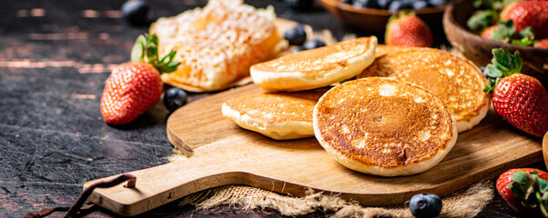 Pancakes on a wooden cutting board with honey and berries.