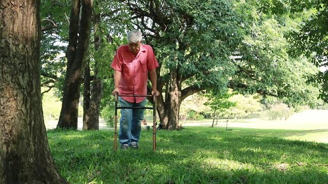 Asian elderly man recovering from paralysis with physiotherapy, using crutches to support his body and walking on the grass, walking slowly to safety.