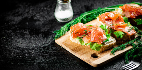 Sandwich with pieces of salmon on a cutting board. 