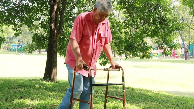 Asian elderly man recovering from paralysis with physiotherapy, using crutches to support his body and walking on the grass, walking slowly to safety.