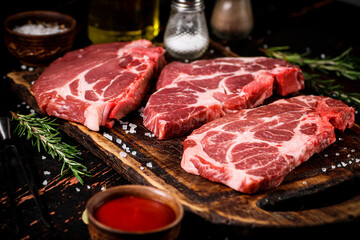 Raw pork steak on a wooden cutting board with tomato sauce and rosemary.