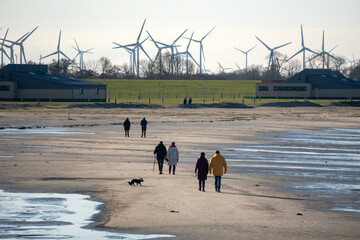 Menschen gehen am Strand der Nordsee spazieren, im Hintergrund eine Gruppe Windräder