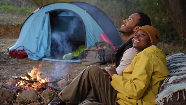 African people spending free time and sitting during camping together on winter day. Young couple of travelers smiling and looking at the sky. Lifestyle moment at nature. Copy space. Slow motion.