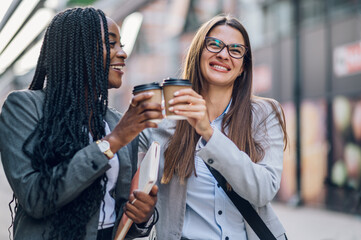 Two multiracial business woman meeting outside and drinking coffee