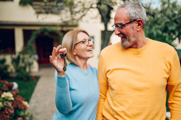 Senior couple holding keys and standing outside their new home