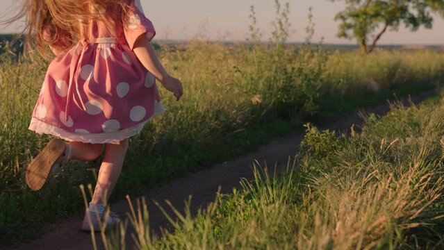 Little happy girl runs on grass, smiles, in slow motion. Kid runs across meadow. Happy running child in field. Happy family. Childhood dream concept. Cheerful child girl playing in park in summer.