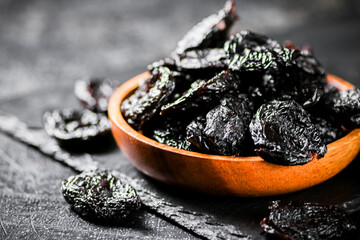 Prunes in a wooden plate on a stone board. 