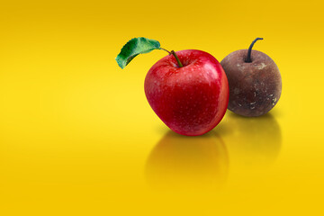 A red apple with a green leaf and a rotten apple behind on a yellow background. The concept of health, life. Choosing the right food.