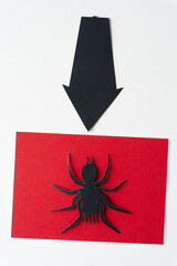 black arrow pointing down to a paper glyph cutout of a spider on a red card