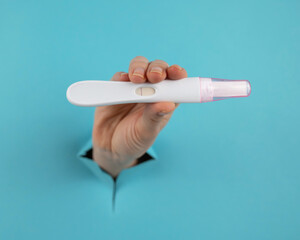 A hand with a negative pregnancy test sticking out of a hole in a blue cardboard background. 