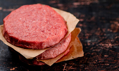 Raw burger on paper. On a rustic dark background.