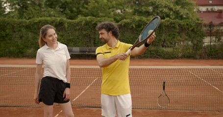 Tennis coach teaching young woman tennis on clay court