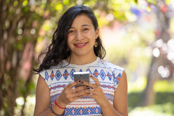 Real Mexican woman holding smart phone and looking at camera outdoors