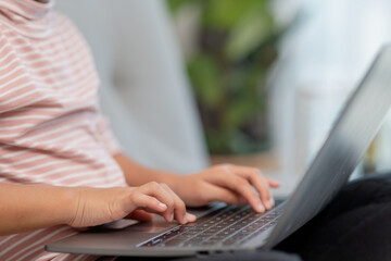 Asian Little school kid girl use laptop computer sitting on sofa alone at home. Child learning reading online social media content, play education lessons game chatting with friends. 