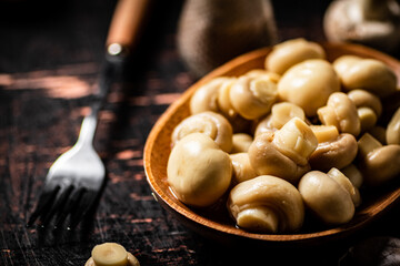 Pickled mushrooms in a wooden plate on the table. 