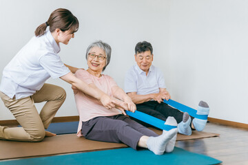 Obraz premium 老人ホームでチューブトレーニング・リハビリするシニア・高齢者の男女と理学療法士・介護士・トレーナー
