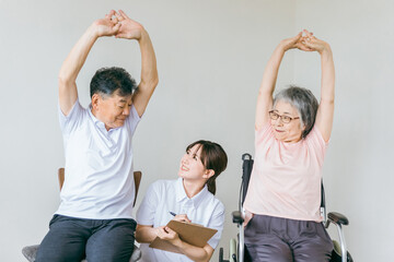 介護施設で椅子体操・運動・リハビリするシニア・高齢者の男女と理学療法士・介護士・トレーナー
