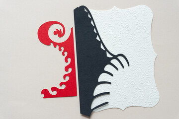 two cut paper decorative shapes (one red and one black) with curvy edges and textured card with damask pattern