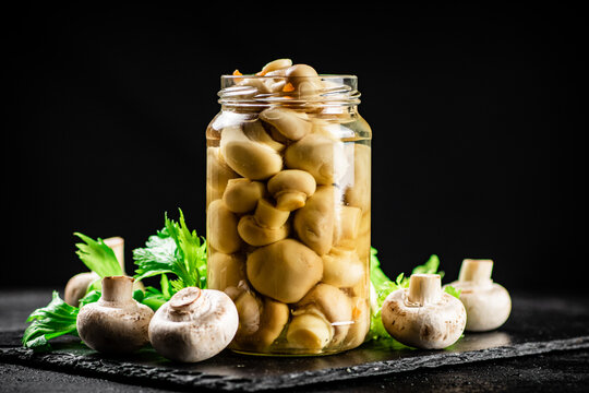 Pickled mushrooms in a jar with greens on a stone board. 
