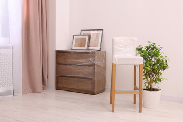 Picture frames, chair and chest of drawers wrapped in stretch film indoors