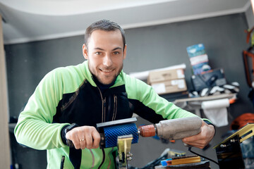 Happy male athlete prepares sliding surface of cross-country skis for winter sports competitions,...