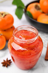 Fototapeta na wymiar Jar of tasty persimmon jam and ingredients on white marble table, above view