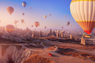 Red car cabriolet in Cappadocia with colorful hot air balloon fly in sky over deep canyons,...