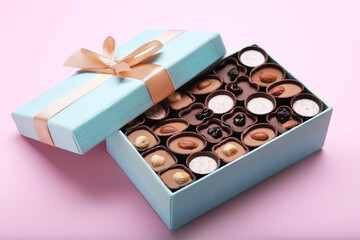 Open box of delicious chocolate candies on pink background, closeup