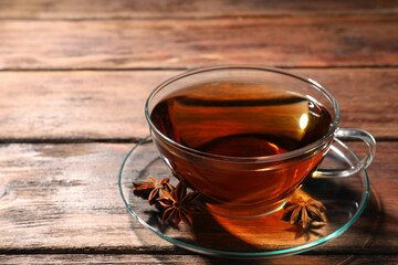 Glass cup of aromatic tea with anise stars on wooden table. Space for text