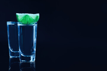 Shot glasses of vodka with lime slice on dark background, space for text