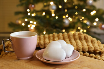 Obraz na płótnie Canvas Cup of delicious cocoa and cookies on wooden table against blurred Christmas tree with lights