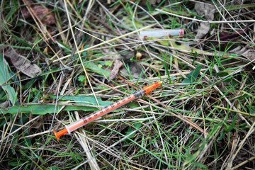 Empty disposable syringe with needle on green grass outdoors