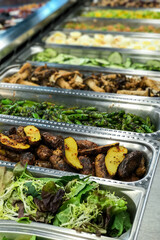 Spring mix of lettuce and leafy greens, roasted fingerling potatoes, and roasted and seasoned edamame at a salad and food bar.
