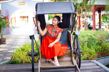 Asian woman in red traditional chiness dress sit at rest room,hand hold red envelope,oranges basket at side,feel happy and hope in happy chinese new year