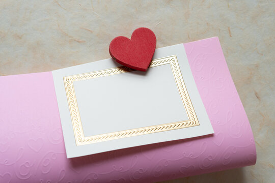 folded pink paper and invitation card with wooden heart painted pink