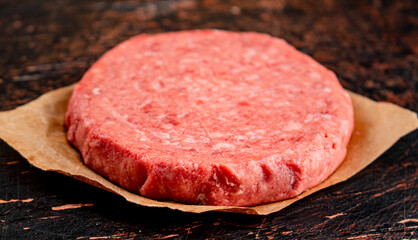 Raw burger on paper. On a rustic dark background.