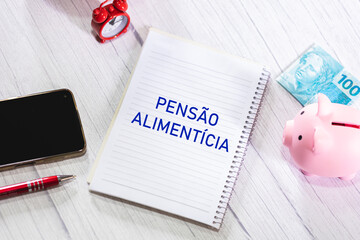 A palavra Pensão Alimentícia em Português do Brasil escrita em um caderno que está sobre uma...