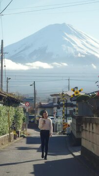 Asian woman enjoy outdoor lifestyle using mobile phone taking picture of mt Fuji covered with snow and local train running cross the street during travel small town in Japan in autumn holiday vacation