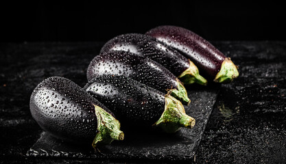 Fresh ripe eggplant with droplets of water on a stone board. 