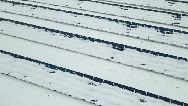 Aerial view of snow covered sustainable electric power plant with many rows of solar photovoltaic panels for producing clean electrical energy. Low effectivity of renewable electricity in winter