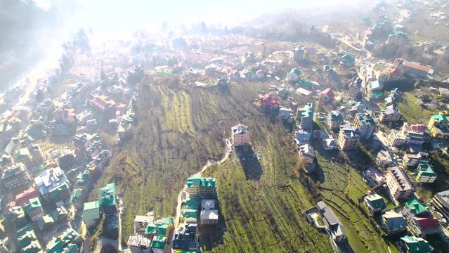 aerial drone shot panning up to reveal kullu manali valley covered in fog from houses and feilds to himalaya mountains in the background peaceful shot of tourist destination in winter