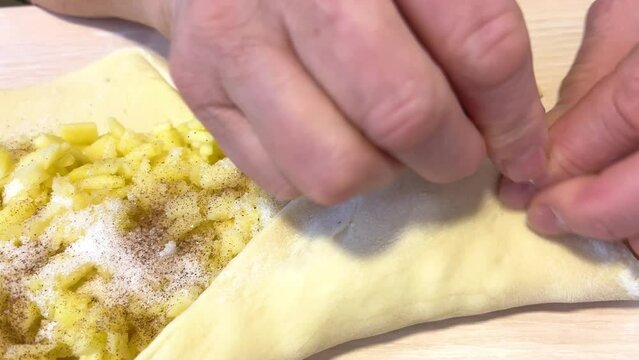hands of an adult woman mold an apple pie from yeast dough a woman glues pieces of dough pouring apples inside for sugar cinnamon finely chopped fruits grandmother prepares pastries for grandchildren