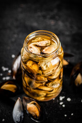 A glass jar with pickled mussels on the table. 