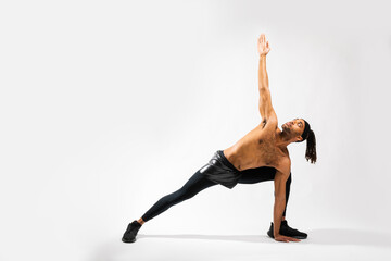 Young flexible Black man doing yoga triangle pose with bent knee on white background in an indoor studio