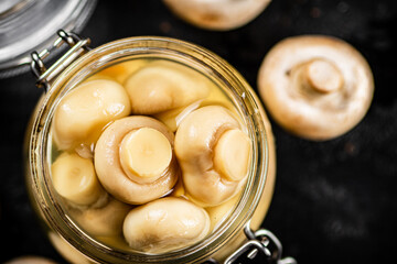 Delicious pickled mushrooms in a small glass jar on the table. 