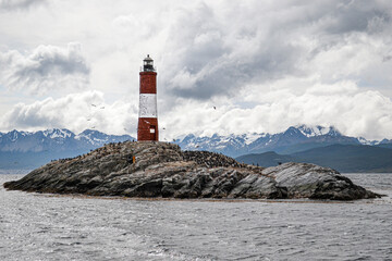 Island with lighthouse and penguins surrounded by snowy mountains